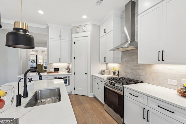 kitchen with visible vents, a sink, stainless steel appliances, light wood-style floors, and wall chimney range hood