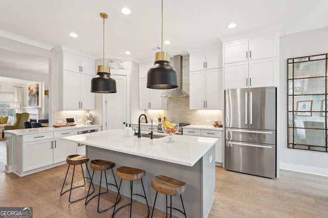 kitchen with light wood finished floors, tasteful backsplash, freestanding refrigerator, wall chimney exhaust hood, and a sink