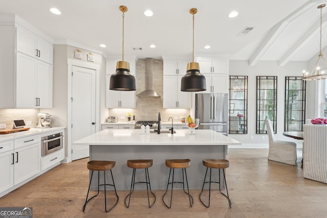 kitchen featuring visible vents, appliances with stainless steel finishes, a kitchen bar, wall chimney exhaust hood, and backsplash