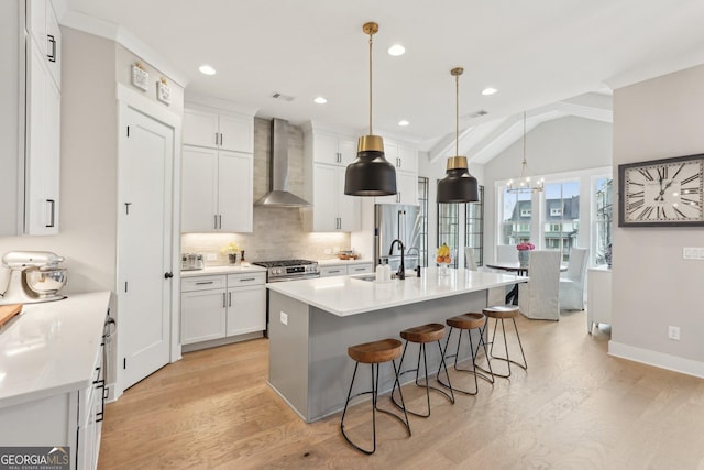 kitchen featuring a sink, white cabinetry, a breakfast bar area, and wall chimney range hood