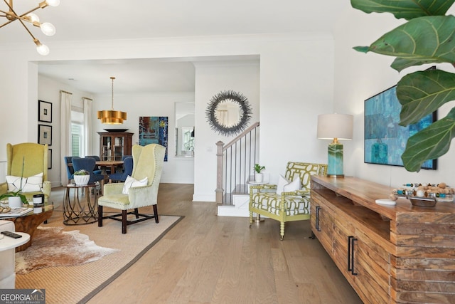 living area with baseboards, a notable chandelier, wood finished floors, and ornamental molding