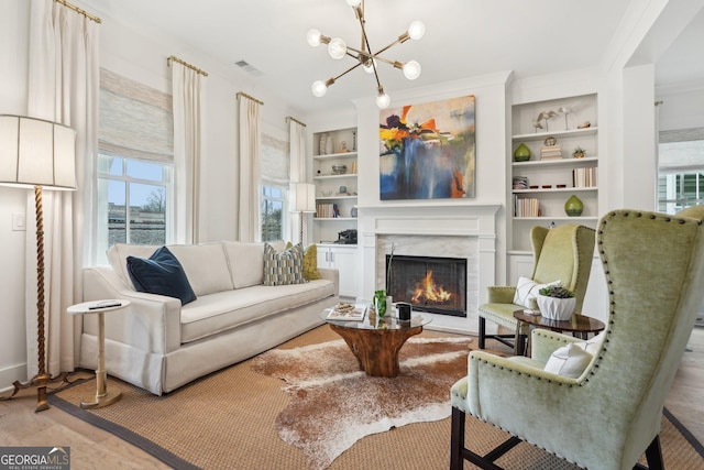 living room featuring visible vents, ornamental molding, built in features, an inviting chandelier, and a premium fireplace