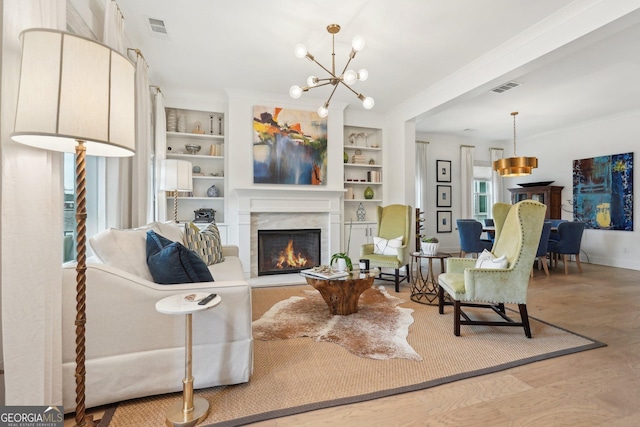 living area featuring visible vents, built in shelves, a warm lit fireplace, wood finished floors, and a chandelier