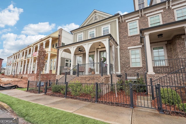 view of front of house featuring brick siding, board and batten siding, ceiling fan, a fenced front yard, and a porch