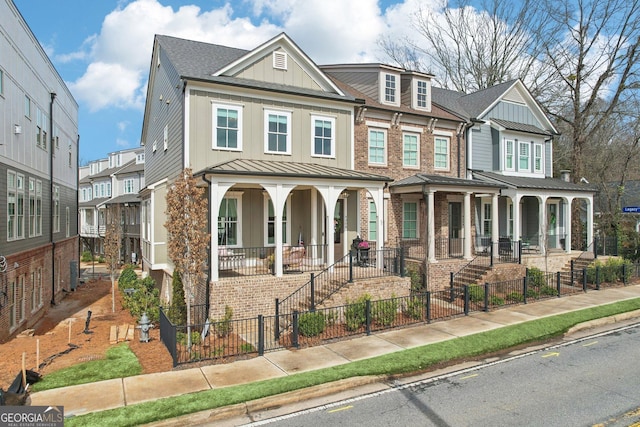 townhome / multi-family property with a standing seam roof, a fenced front yard, a porch, board and batten siding, and brick siding