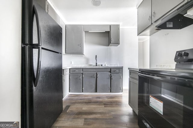 kitchen featuring gray cabinetry, a sink, range hood, dark wood-style floors, and black appliances