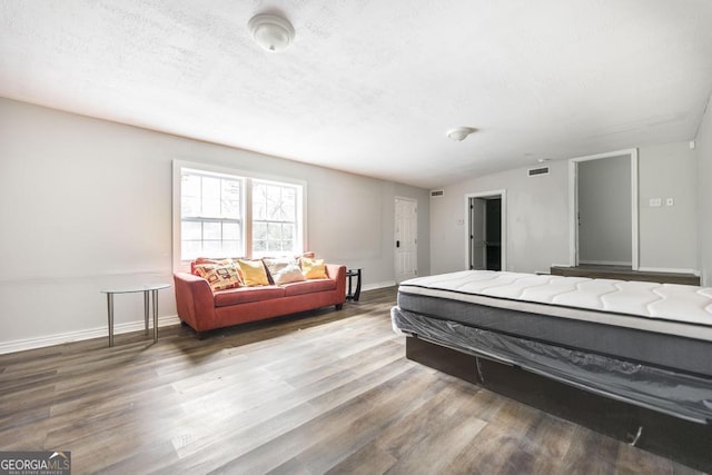 bedroom featuring lofted ceiling, visible vents, a textured ceiling, wood finished floors, and baseboards