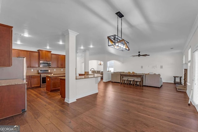 kitchen with arched walkways, dark wood finished floors, brown cabinets, stainless steel appliances, and crown molding