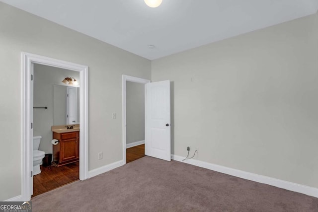 unfurnished bedroom with baseboards, dark colored carpet, a sink, and ensuite bathroom