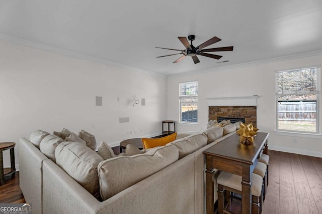 living area featuring ornamental molding, dark wood-style flooring, a stone fireplace, and a ceiling fan