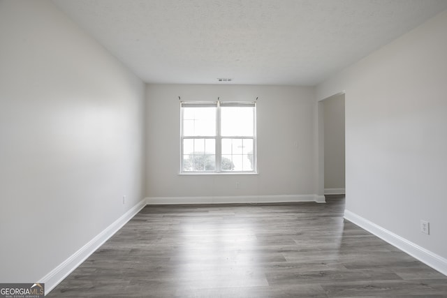 unfurnished room featuring dark wood-style floors, visible vents, a textured ceiling, and baseboards