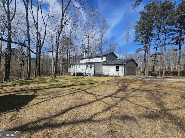 view of property exterior with driveway, an attached garage, a chimney, and a yard