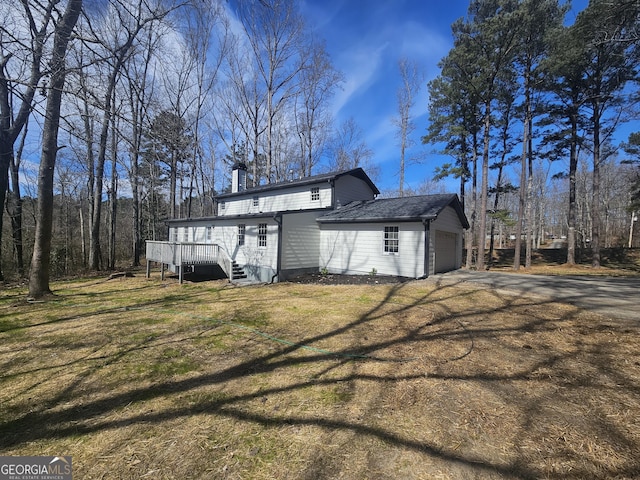 exterior space with a deck, an attached garage, a yard, driveway, and a chimney