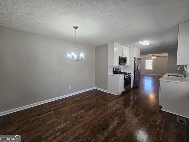 kitchen with ceiling fan with notable chandelier, stainless steel appliances, a sink, light countertops, and dark wood-style floors