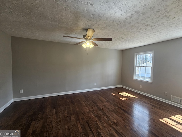 spare room with dark wood-style flooring, visible vents, ceiling fan, and baseboards