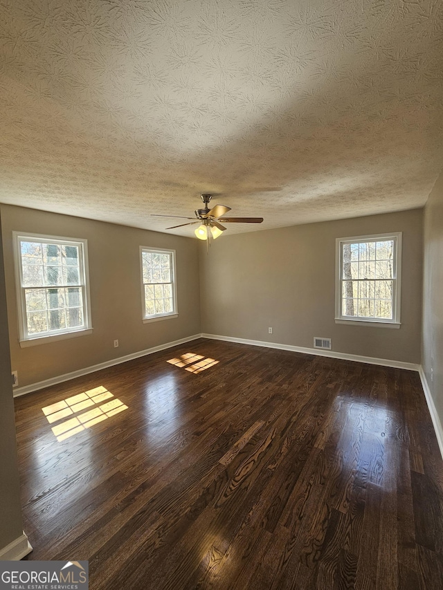 spare room with dark wood-style floors, visible vents, ceiling fan, a textured ceiling, and baseboards