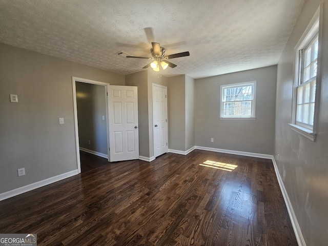 unfurnished bedroom with ceiling fan, a textured ceiling, baseboards, and dark wood-type flooring