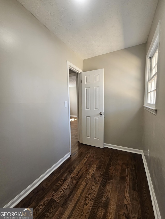 unfurnished bedroom featuring baseboards, dark wood finished floors, and a textured ceiling