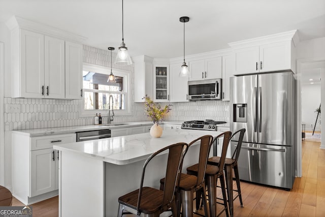 kitchen featuring light stone counters, light wood-style flooring, stainless steel appliances, white cabinetry, and a sink