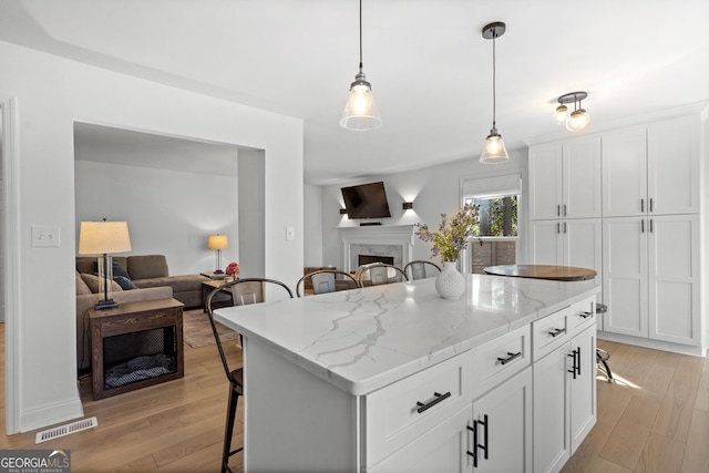 kitchen with light wood-type flooring, visible vents, open floor plan, a high end fireplace, and a breakfast bar area