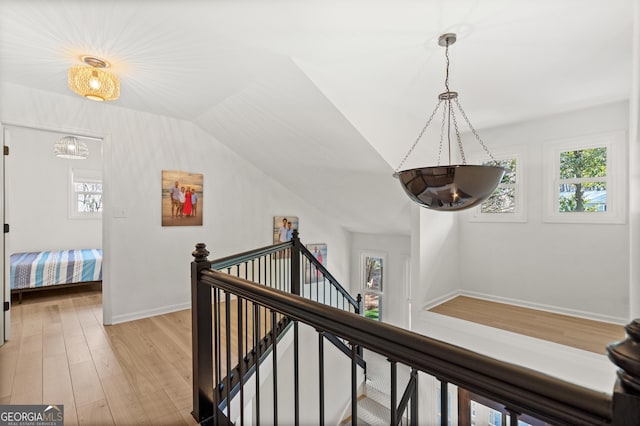 corridor featuring lofted ceiling, an upstairs landing, baseboards, and light wood finished floors