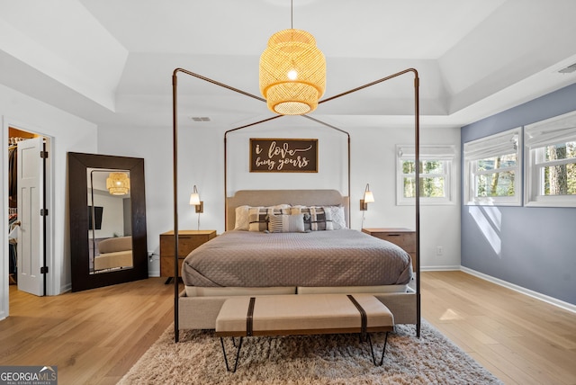 bedroom with baseboards, a raised ceiling, and wood finished floors