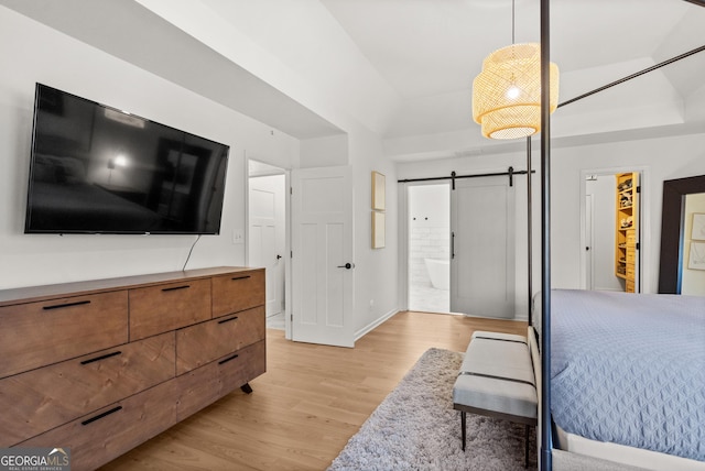 bedroom featuring baseboards, ensuite bath, light wood-style floors, and a barn door