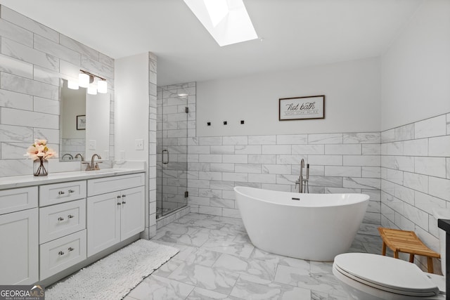 full bath featuring vanity, a soaking tub, a skylight, tile walls, and marble finish floor