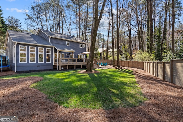 rear view of house featuring a yard, a fenced backyard, crawl space, a deck, and a trampoline