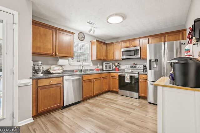 kitchen featuring light wood finished floors, visible vents, appliances with stainless steel finishes, brown cabinets, and a sink