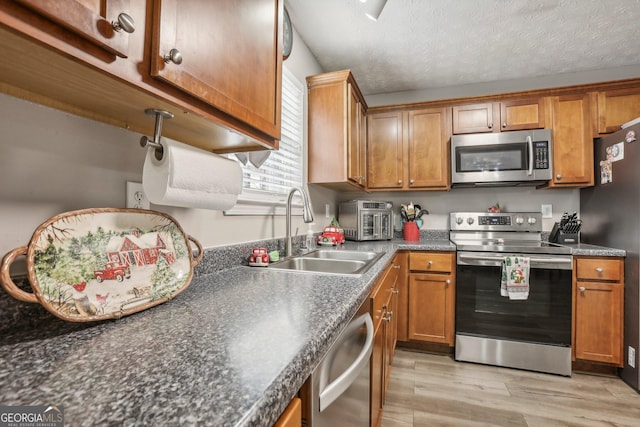 kitchen with appliances with stainless steel finishes, brown cabinetry, and a sink