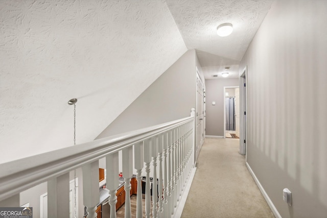 corridor with light colored carpet, vaulted ceiling, a textured ceiling, and baseboards