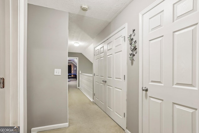 hallway with light carpet, vaulted ceiling, and a textured ceiling