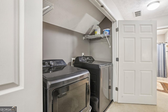 clothes washing area with washer and dryer, laundry area, visible vents, and a textured ceiling