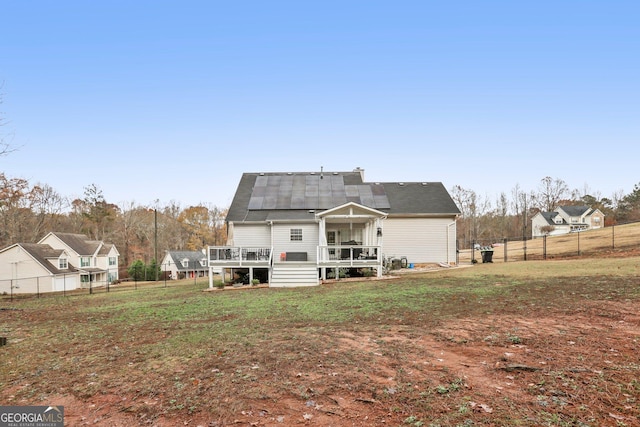 rear view of property featuring a lawn, fence, a wooden deck, and roof mounted solar panels