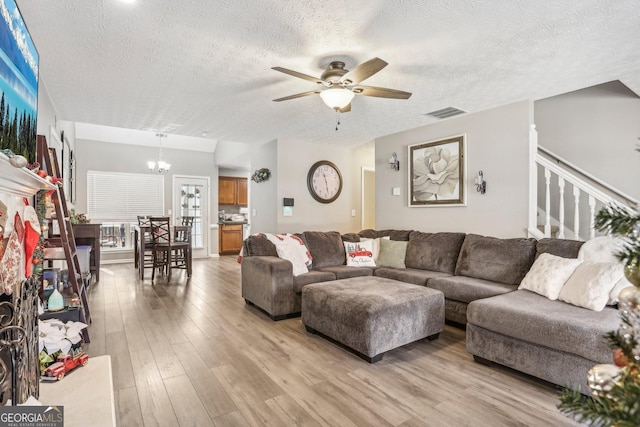 living room featuring light wood finished floors, visible vents, stairway, a textured ceiling, and ceiling fan with notable chandelier