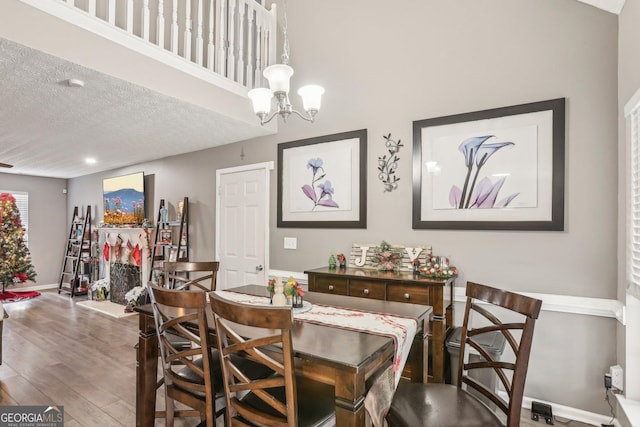 dining space featuring baseboards, a textured ceiling, a chandelier, and wood finished floors