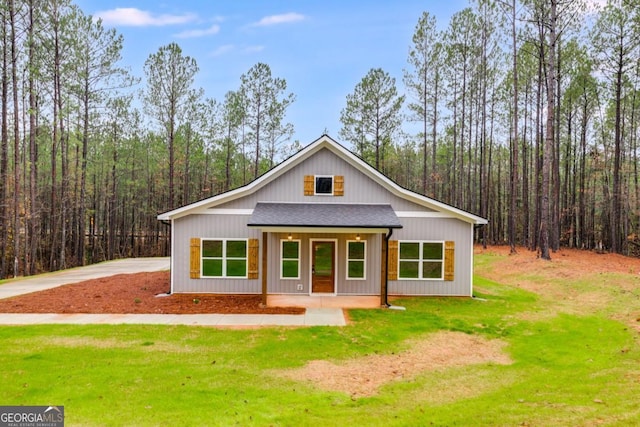 view of front of property featuring a shingled roof, a front yard, a porch, and a wooded view