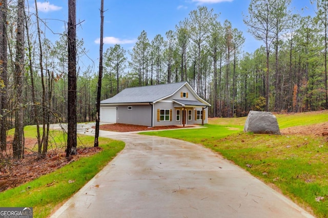 view of front of house with a view of trees, concrete driveway, and a front yard