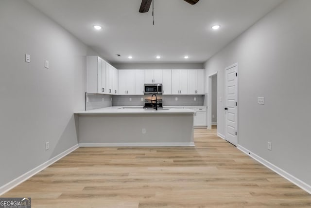 kitchen with white cabinets, decorative backsplash, stainless steel microwave, a peninsula, and light countertops