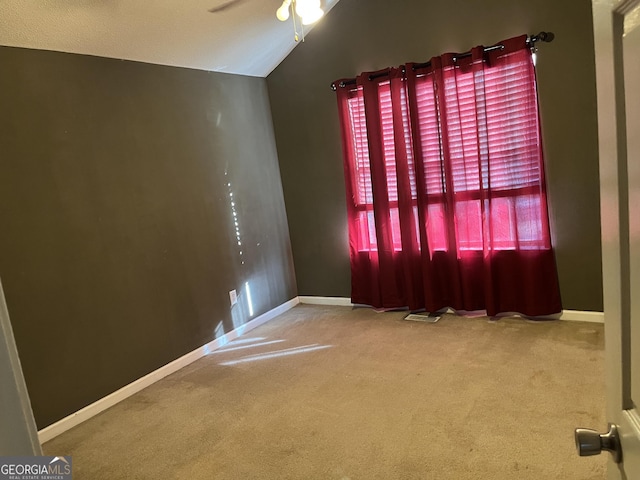 empty room featuring vaulted ceiling, carpet floors, ceiling fan, and baseboards