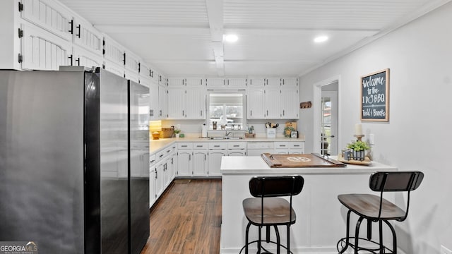 kitchen with dark wood-style flooring, freestanding refrigerator, a peninsula, a kitchen bar, and white cabinetry