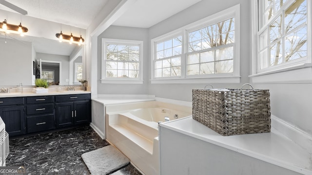 full bath featuring double vanity, a garden tub, a textured ceiling, and a sink