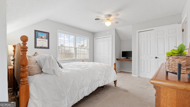 carpeted bedroom featuring multiple closets, visible vents, vaulted ceiling, and a textured ceiling