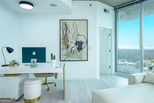 home office with baseboards, visible vents, floor to ceiling windows, and wood finished floors