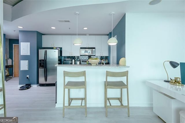 kitchen featuring stainless steel appliances, visible vents, a kitchen breakfast bar, hanging light fixtures, and tasteful backsplash