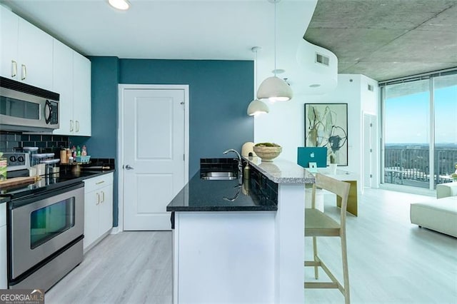 361 17th St Unit 2122, Atlanta, GA 30363 - kitchen with appliances with stainless steel finishes, light wood finished floors, a kitchen bar, decorative backsplash, and white cabinetry