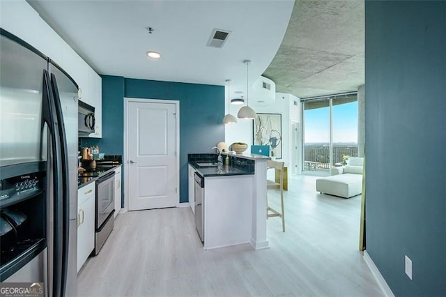 kitchen featuring a peninsula, appliances with stainless steel finishes, light wood-type flooring, dark countertops, and a kitchen bar