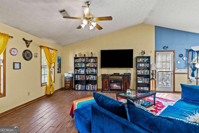 living area featuring visible vents, a glass covered fireplace, wood finished floors, vaulted ceiling, and a healthy amount of sunlight