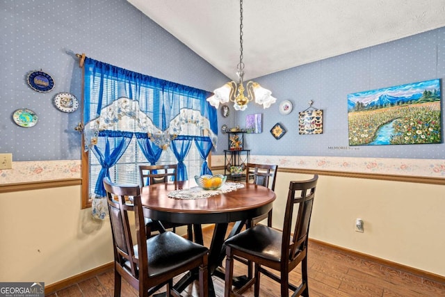 dining space with lofted ceiling, wood-type flooring, baseboards, and a notable chandelier